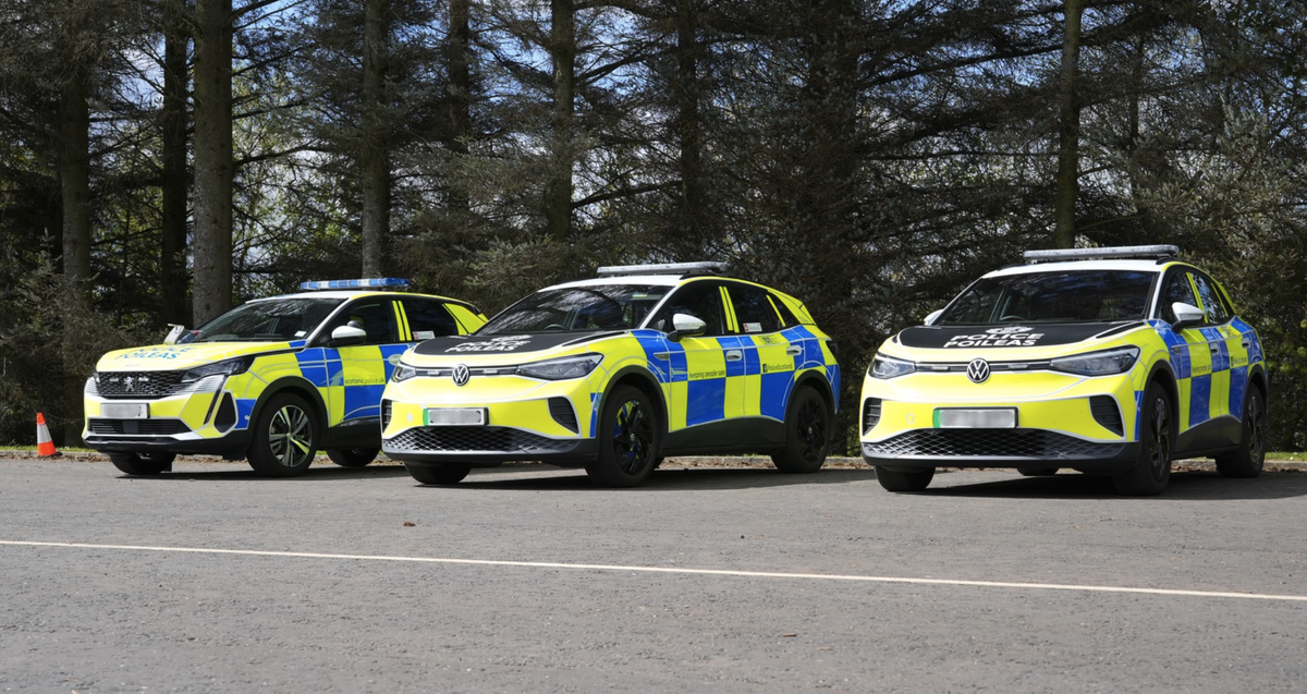 A row of three police cars side by side in front of some trees. 