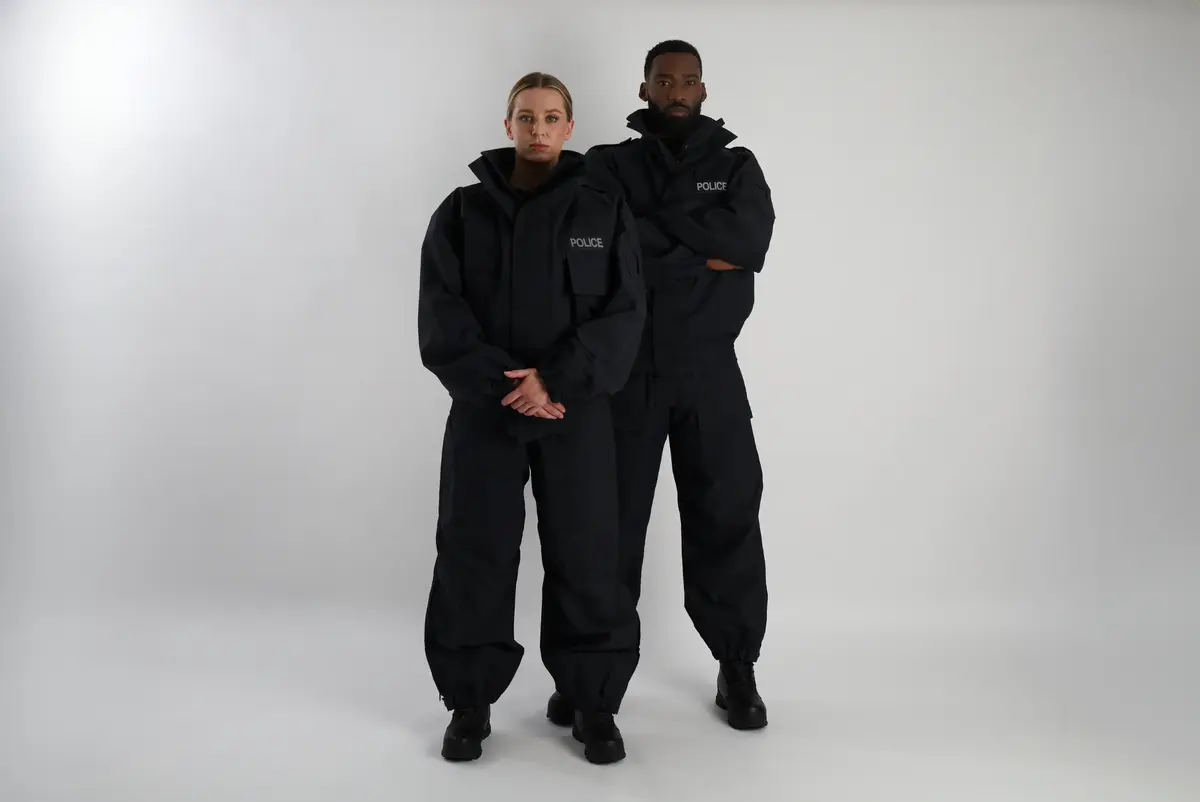 Two Police officers wearing protective suits stood looking towards the camera with a plain background. 