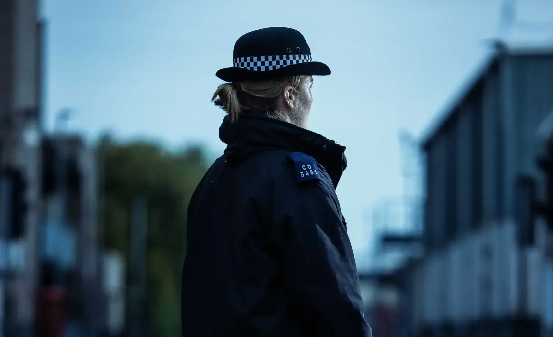 The back of a police officer stood in uniform outside. 